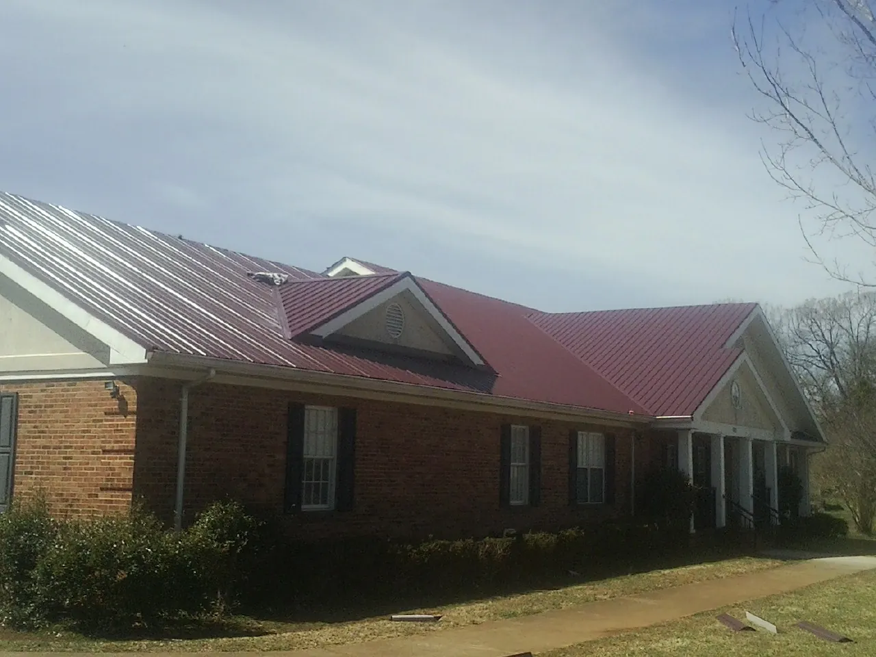 Red metal roof with gabled entries on a long brick building, from a Hail Damage Roof Repair job in Gully