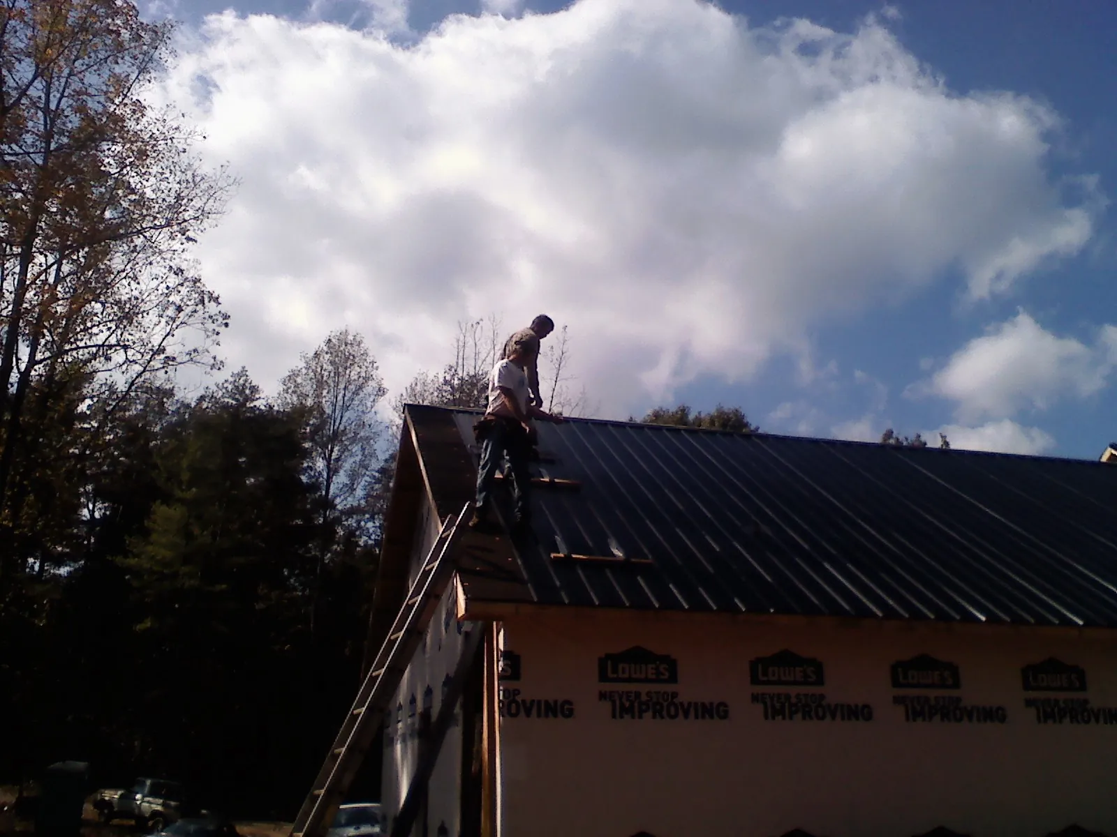 Roofer fastening dark metal panels high against a cloudy sky, from a Roof Inspection job in Gully