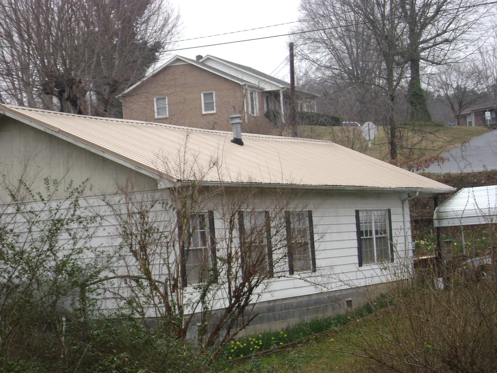 Tan metal roof on a white sided house set into a hillside — Commercial Roofing by Roofing Brothers in Gully