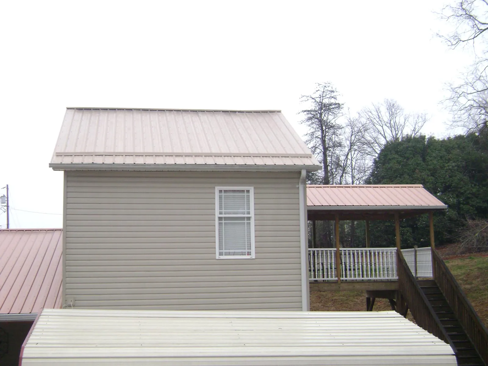 Tan metal roofs on a two story addition and attached porch, from a Roof Replacement job in Gully